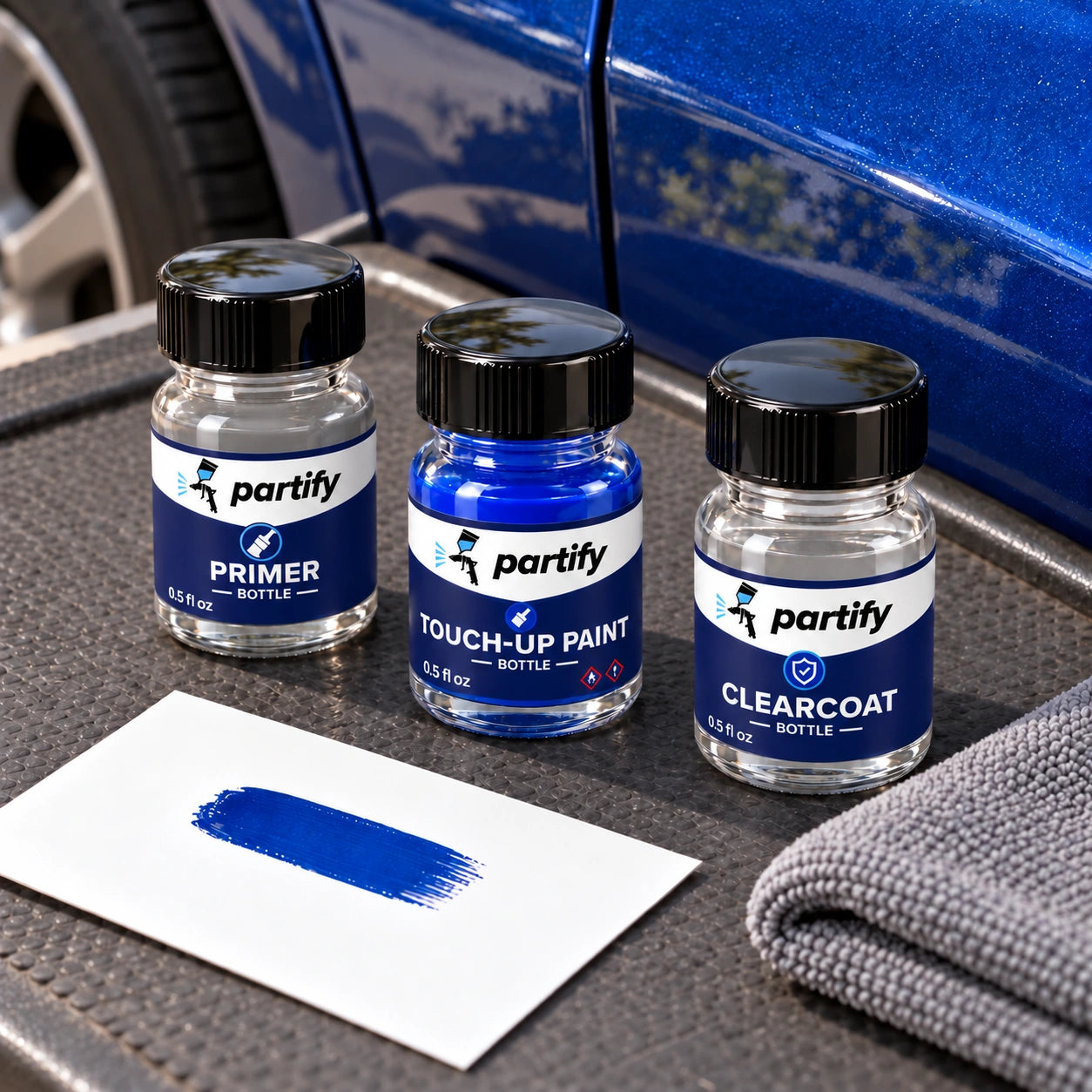 Primer, color and clearcoat bottles with matching dark navy labels arranged on a work mat with a test card and cloth